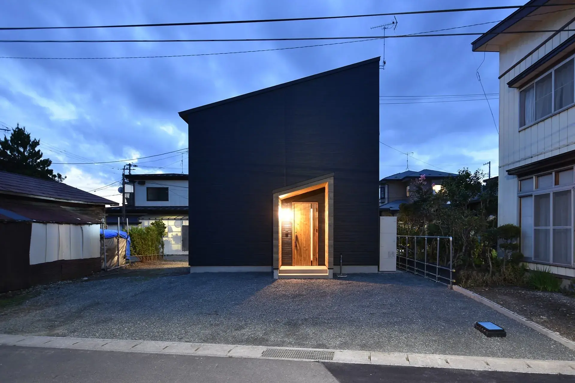 夕暮れに玄関の灯りがともる黒い外壁の家